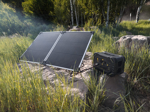 RECERTIFIED - Lion Summit portable power station with two solar panels on rocks in tall grass, providing off-grid power