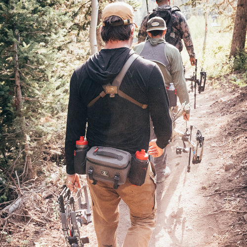 Two individuals hiking through a forest with hunting gear and both wearing park packs.