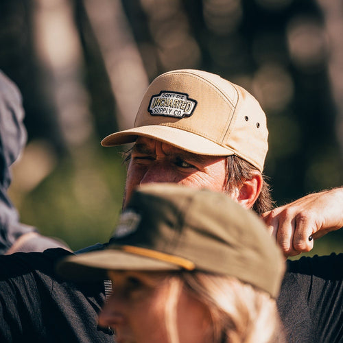 Navigator Hat: man wearing tan Uncharted Supply Co. outdoor cap with logo patch, visible eyelets