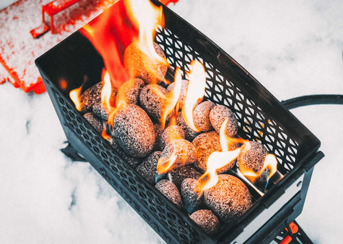 Ignik FireCan Rocks, dark lava rocks burning in a black portable propane fire pit, surrounded by snow