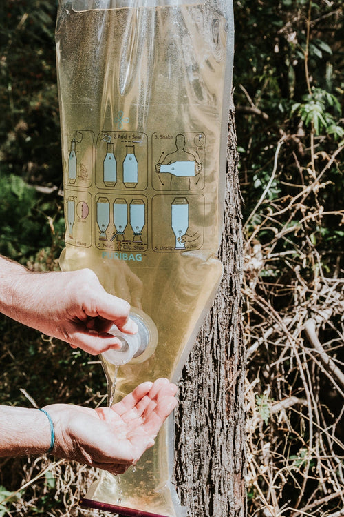 Puribag Bug out pack, purified water flowing from portable emergency water filter bag into cupped hands
