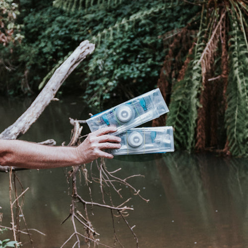 Puribag 2-Pack clear water purification bags held over a river, ready for outdoor survival or emergency use