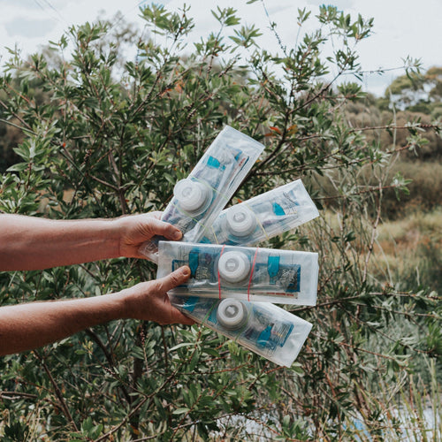 Puribag Bug out pack 4-Pack held by hands in a lush green outdoor setting, for emergency water purification