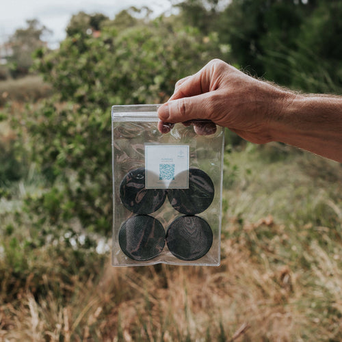 Puribag Filter Replacement Pack: hand holding clear bag with 4 dark circular water filter refills against outdoor foliage