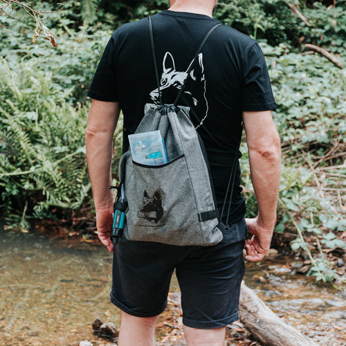 Puribag Pro Kit water filtration system attached to a gray drawstring bag worn by person by stream
