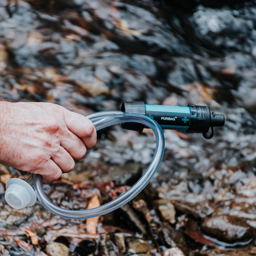 Puribag Pro System portable water filter held by hand, drawing water from a stream