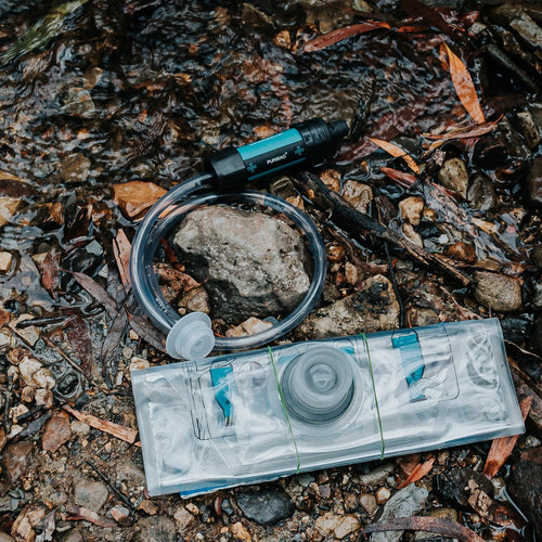 Puribag Pro System black water filter with clear tubing and collapsible reservoir bag in a shallow stream
