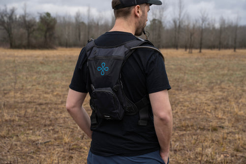 Puribag Adventure Pack black hydration backpack with blue logo and tube worn by man in a field