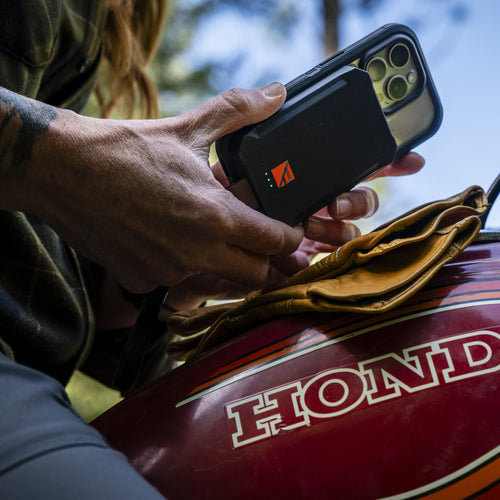 Dark Energy Poseidon Nano portable power bank charging a phone, held by a person on a Honda motorcycle