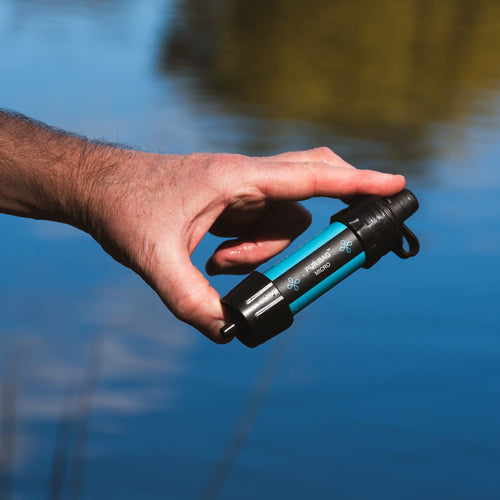 Puribag Pro - Membrane Filter Kit, turquoise and black portable water filter held by hand over outdoor water