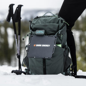 Spectre 8W portable solar panel and power bank by Dark Energy, attached to a tactical backpack in fresh snow