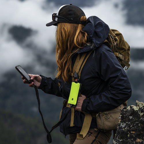 Dark Energy Poseidon Pro neon yellow rugged power bank charging phone while worn by a hiker on a misty mountain trail