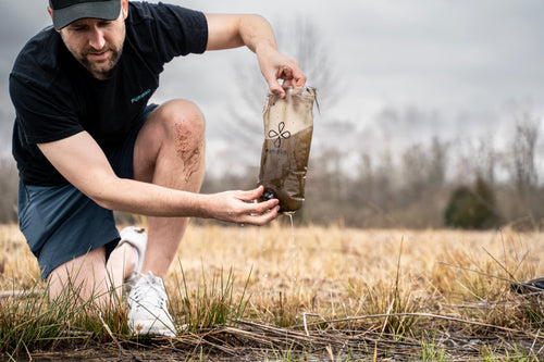 Puribag Adventure Pack: Man filters murky water from a clear Puribag in a marshy area, clean water drips from filter