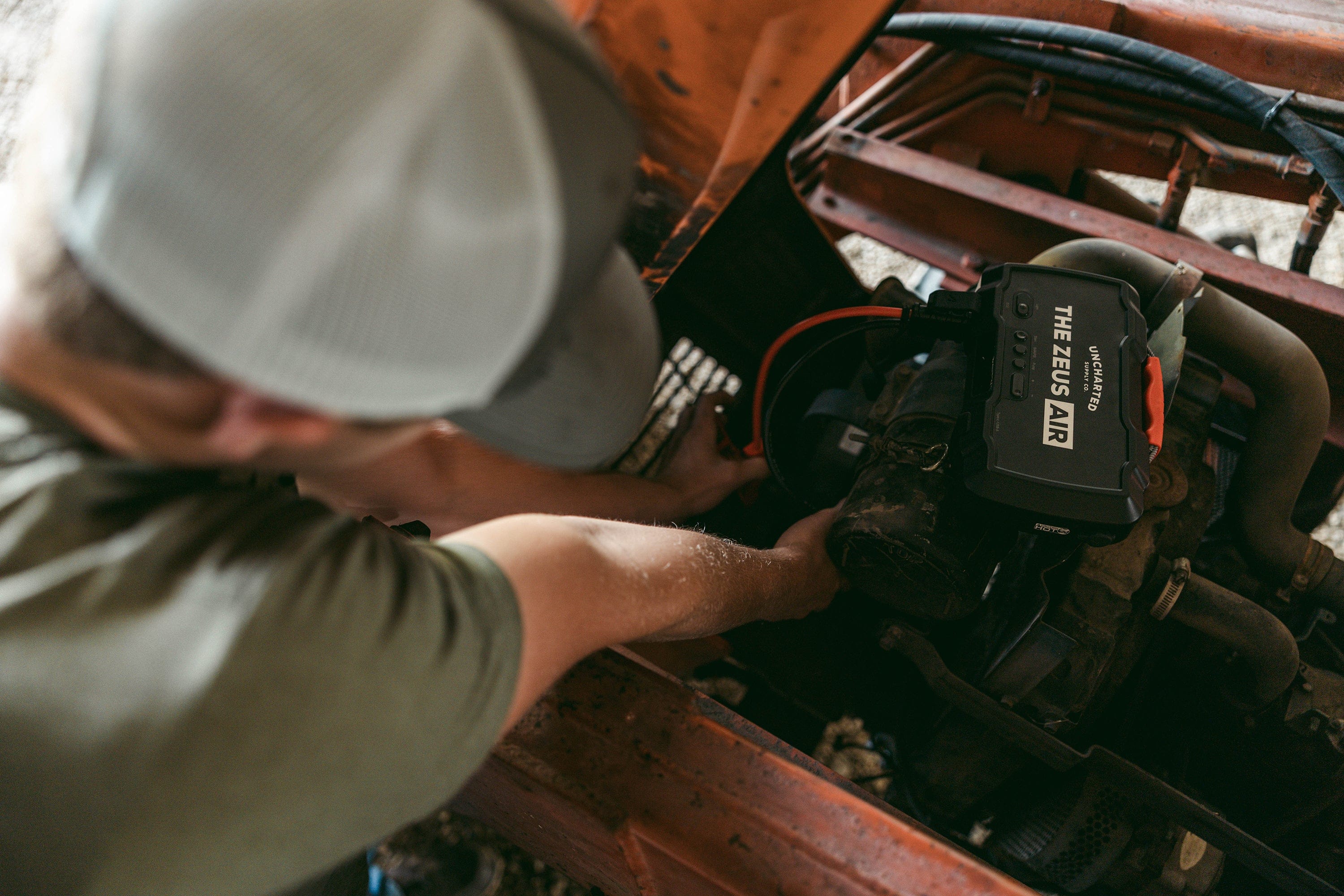 Person using Uncharted Zeus Air portable jump starter and air compressor on a vehicle engine