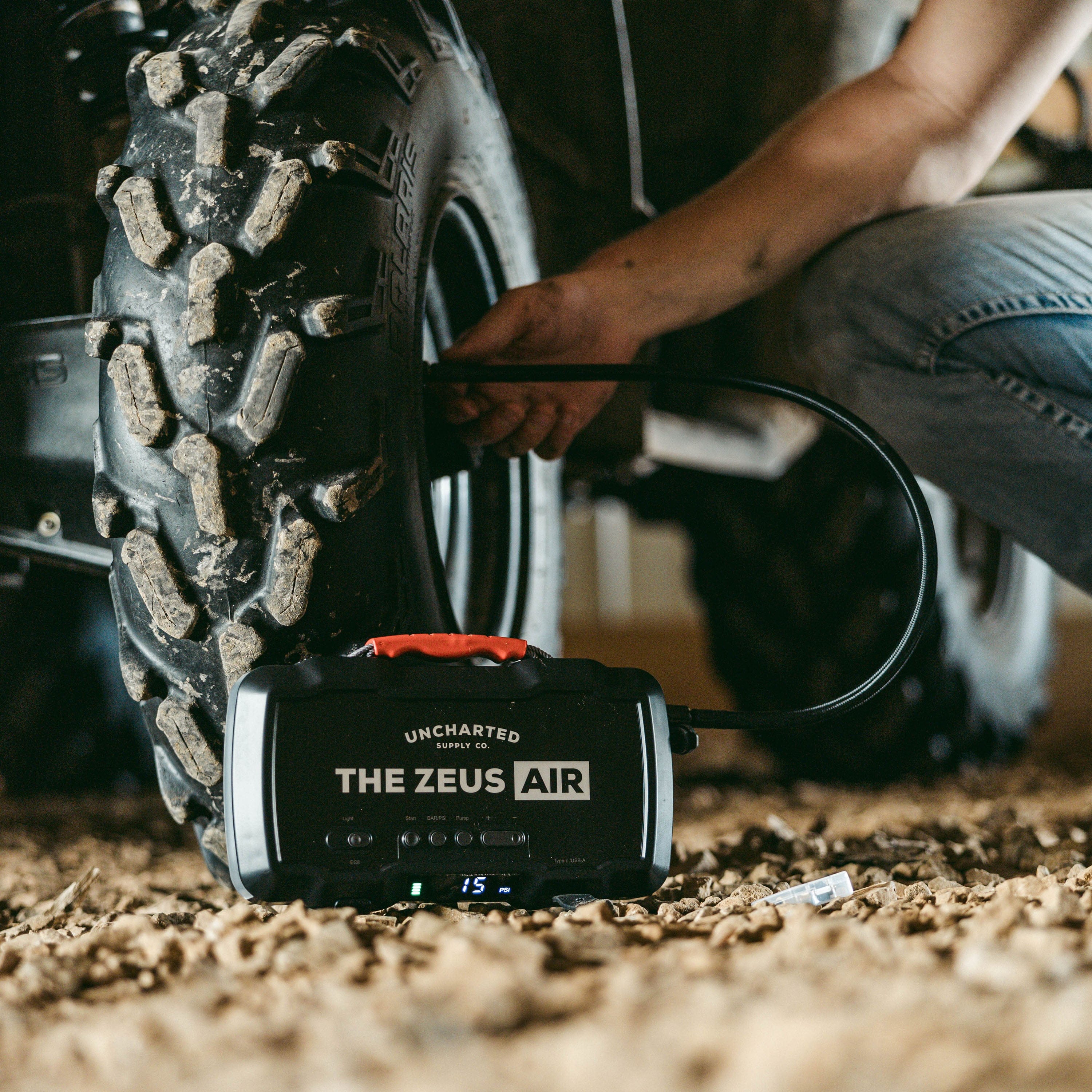 Uncharted Zeus Air portable air compressor inflating an ATV tire, a person connecting the hose, 15 PSI displayed
