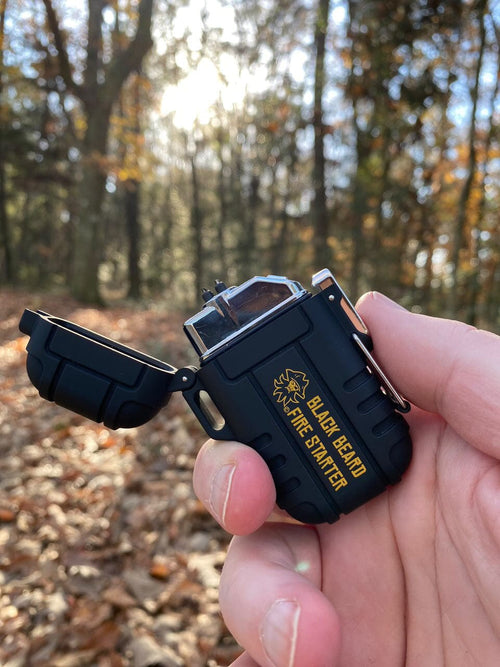 Black Beard Arc Lighter, open in a hand, rugged black casing with 'Fire Starter' gold text, outdoor forest background