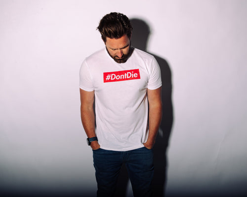 The Hashtag men's white #DontDie t-shirt, a survival apparel graphic tee worn by a man looking down