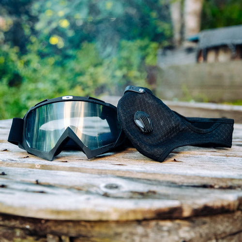 Safety goggles with reflective lenses and a black tactical dust mask on rustic outdoor wooden planks