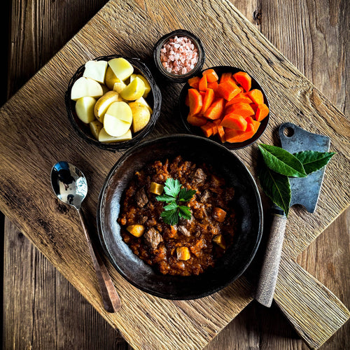 BISON STEW, a hearty ready-to-eat meal with potatoes, carrots, and salt, served on a rustic wooden board