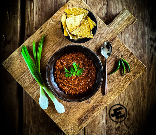 Essential Provisions ready-to-eat chili meal with tortilla chips, green onions, and peppers on a rustic wood board