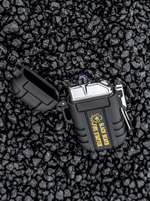 Black Beard Arc Lighter, black with gold 'Black Beard Fire Starter' text, showing purple arc on dark pebbles