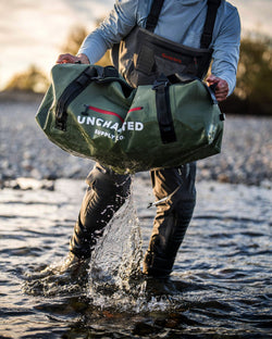 Uncharted Supply Co. waterproof Vault duffel carried by a person wading in a river, water splashing