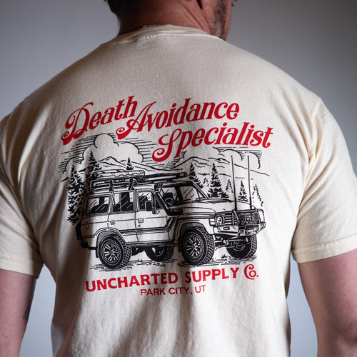 Death Avoidance Specialist T-Shirt on man's back, features off-road vehicle, mountains, trees, Uncharted Supply Co. logo