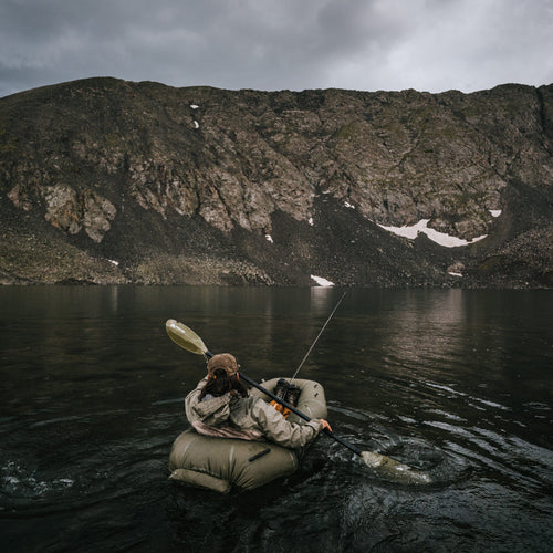 Person in a rapid raft on a lake with a mountainous background