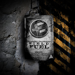 Essential Provisions FIELD FUEL Hearty Bison Chili MRE pouch on a rugged concrete wall with yellow hazard stripes