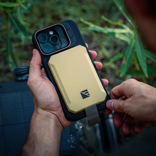 Poseidon Nano rugged tan portable phone charger attached to phone, held by hands outdoors