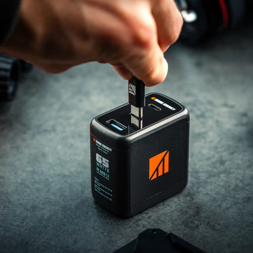 65W Wall Adapter by Dark Energy, a hand plugs a USB-C cable into the dual-port fast charger on a dark surface