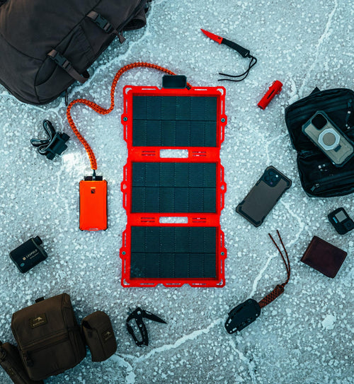 Dark Energy Spectre 18W power bank & red foldable solar panel for emergency power, with outdoor gear on a light, snowy surface