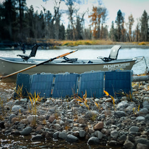 Dark Energy Spectre 56W portable solar panel on a rocky riverbank next to a boat for outdoor charging
