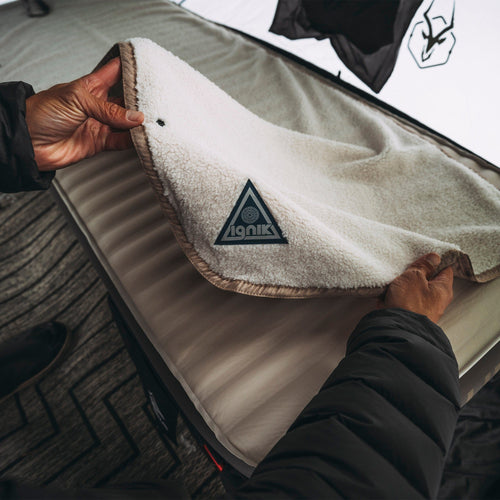 Flipside Heated Bed Cover Fleece by Ignik, person holding a fluffy cream fleece blanket over a camping mattress