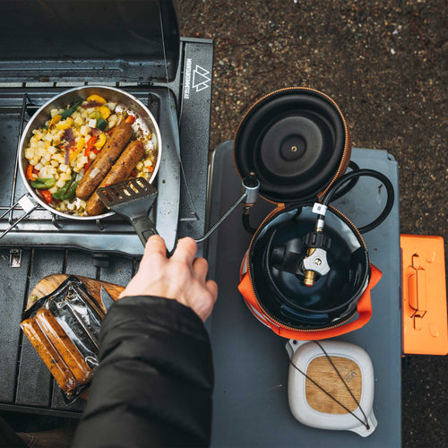 Ignik Gas Growler 3.8 Deluxe portable propane tank connected to a camping stove cooking sausages and vegetables