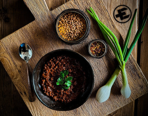Essential Provisions ready-to-eat survival meal: lentil stew, fresh greens & spices on a wooden board