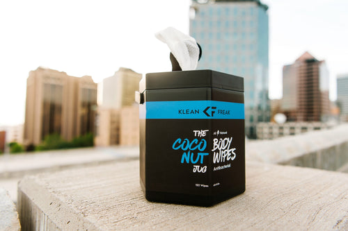 Klean Freak Coconut Body Wipes Jug, black antibacterial container dispensing a wipe in an urban setting