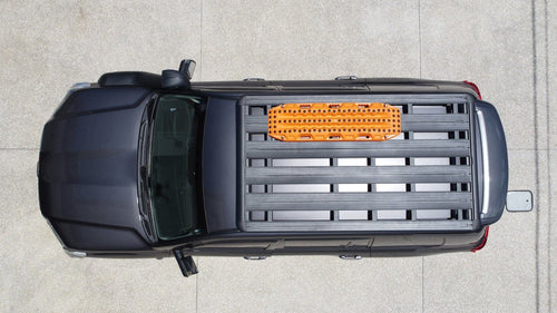 Adventure Imports MAXTRAX Flat Rack Mount holding an orange recovery board on a black SUV roof rack