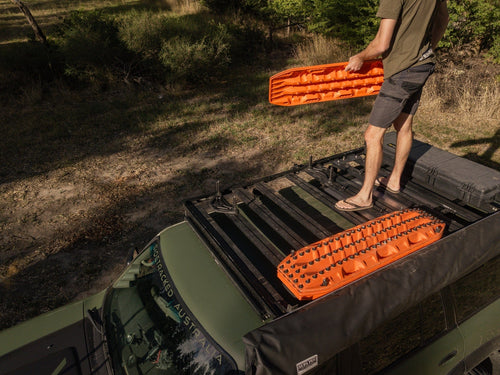 MAXTRAX Flat Rack Mount securely holding orange recovery boards on a green vehicle roof, person installing another board