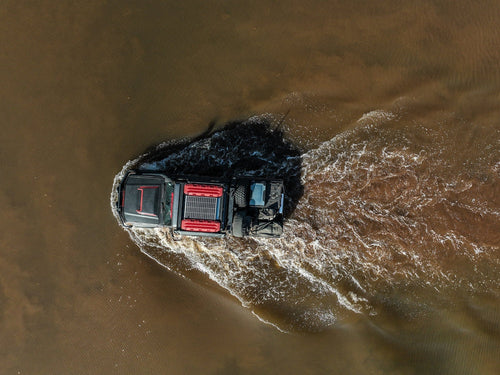 MAXTRAX XTREME Red Recovery Boards by Adventure Imports on an off-road truck crossing muddy water