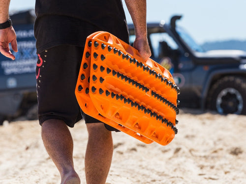 Adventure Imports MAXTRAX XTREME Signature Orange recovery boards held by a person on a beach, SUV in background