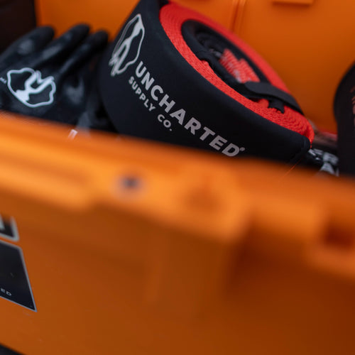 The Extractor - Tow Strap in black and red by Uncharted Supply Co. shown in an orange survival gear kit with gloves