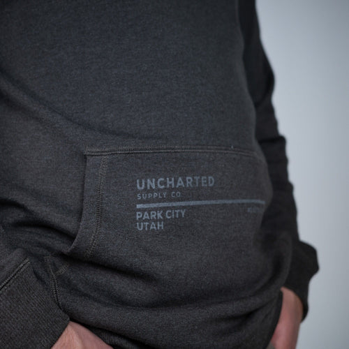 Normal Brand X Uncharted Hoodie in charcoal grey marled fabric, front kangaroo pocket with UNCHARTED logo