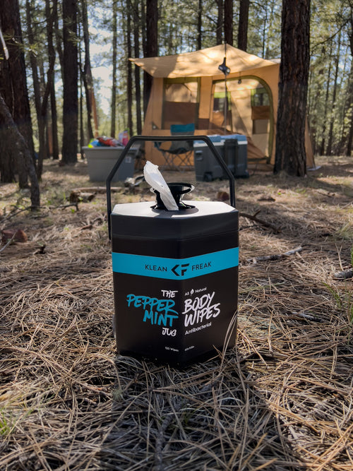 Klean Freak The Peppermint Body Wipes Jug, black hexagonal container with wipe, at a sunny forest campsite
