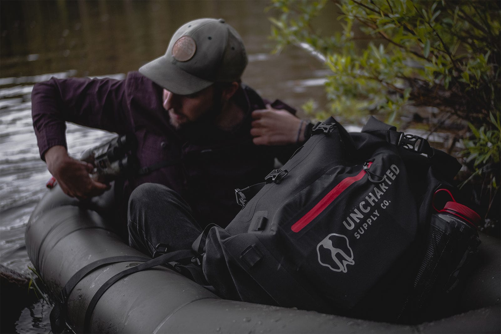 Uncharted Supply Co. dry bag, a black waterproof bag with red accents, in an inflatable boat with a man