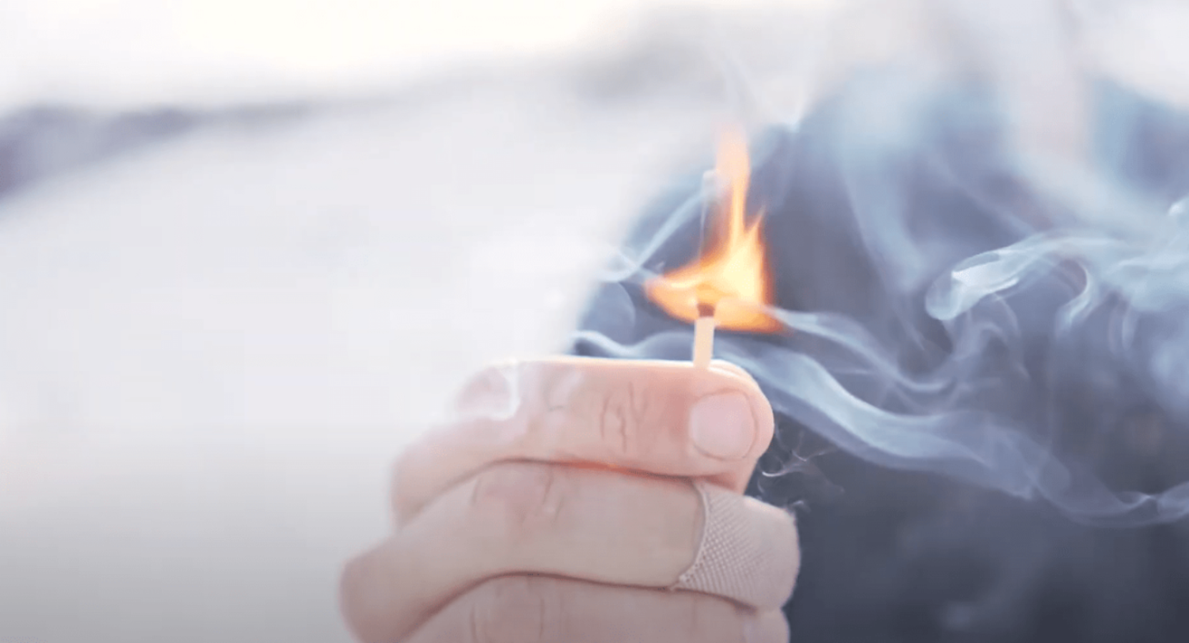 Outdoor survival: hand with bandage holding a lit match with smoke