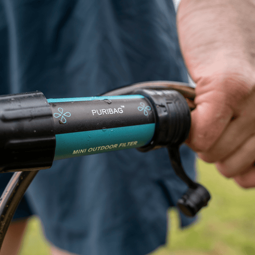 Puribag Pro - Membrane Filter Kit, a black and teal portable outdoor water filter being used