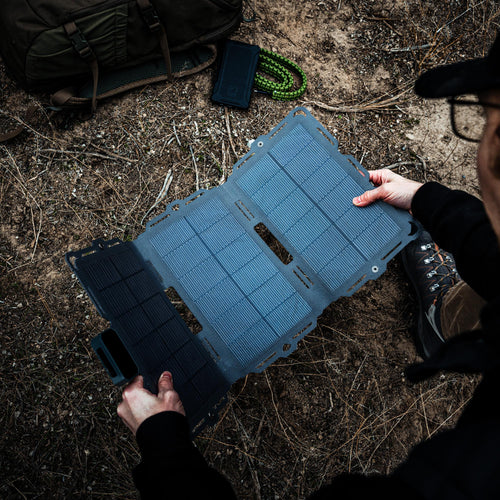 Spectre 18W Dark Energy foldable solar charger deployed outdoors by a person with a backpack and power bank