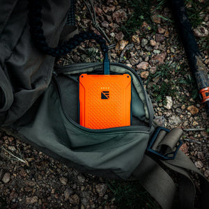 Dark Energy Poseidon Pro orange rugged portable power bank in a backpack pocket, charging outdoors on rocky ground