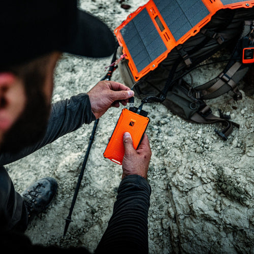 Poseidon Pro rugged power bank by Dark Energy charging from a solar panel on a backpack in a rocky outdoor setting